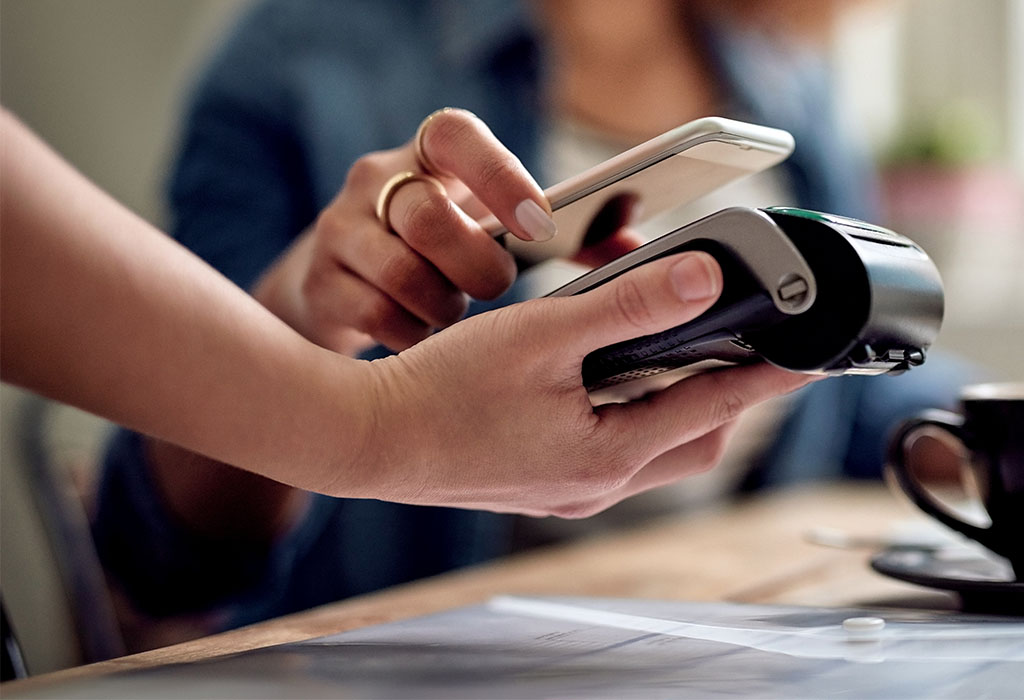 Closeup shot of a woman paying using NFC technology on her phone at a payment terminal EFTPOS in a cafe