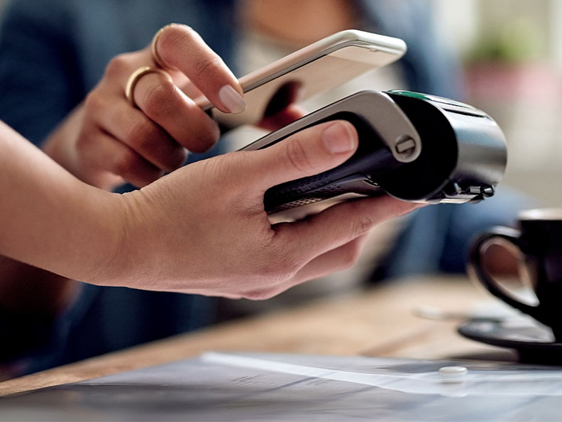 Closeup shot of a woman paying using NFC technology on her phone at a payment terminal EFTPOS in a cafe