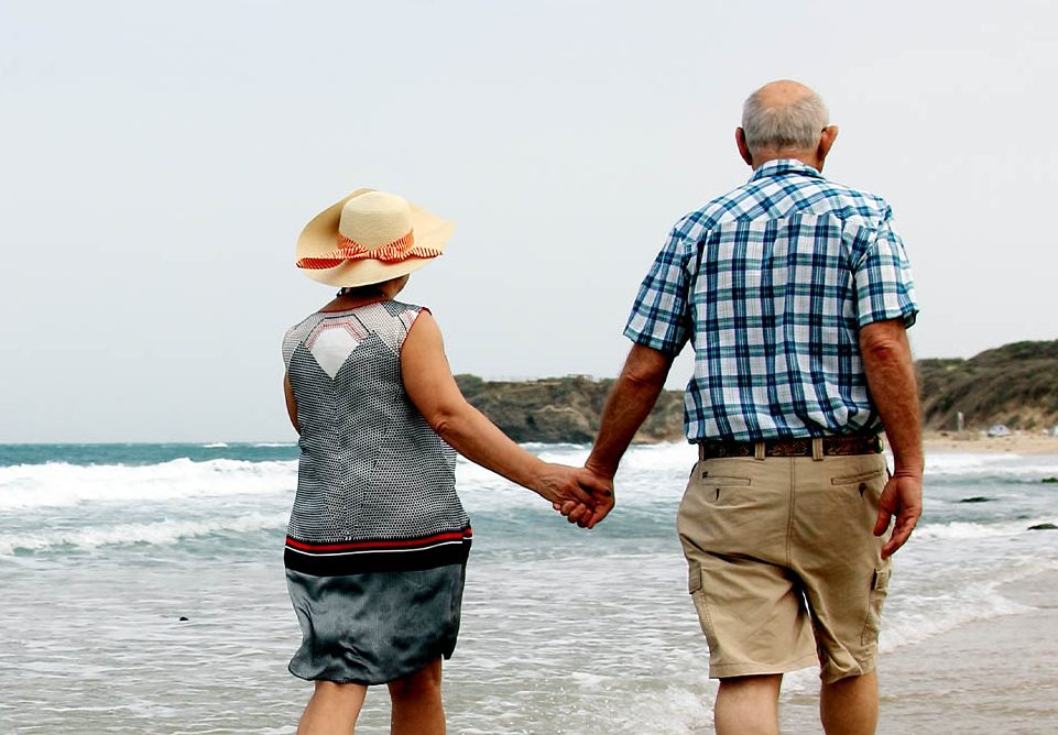 A mature aged couple walks along the water at the beach during a sunny day while holding hands.