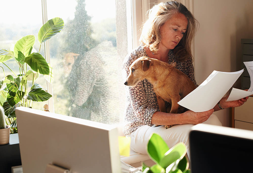 Woman with dog reviewing paperwork in sunny home office