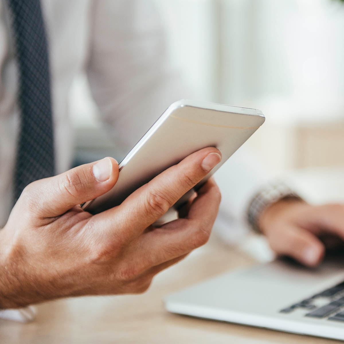 A business man with a tie holding a phone and typing on a laptop