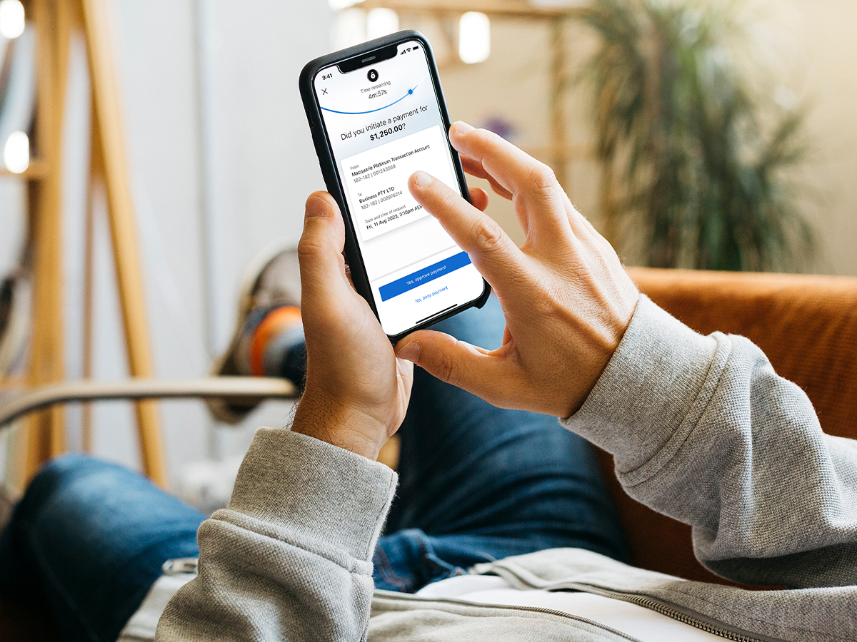 man on couch holding his phone with Macquarie Authenticator app open
