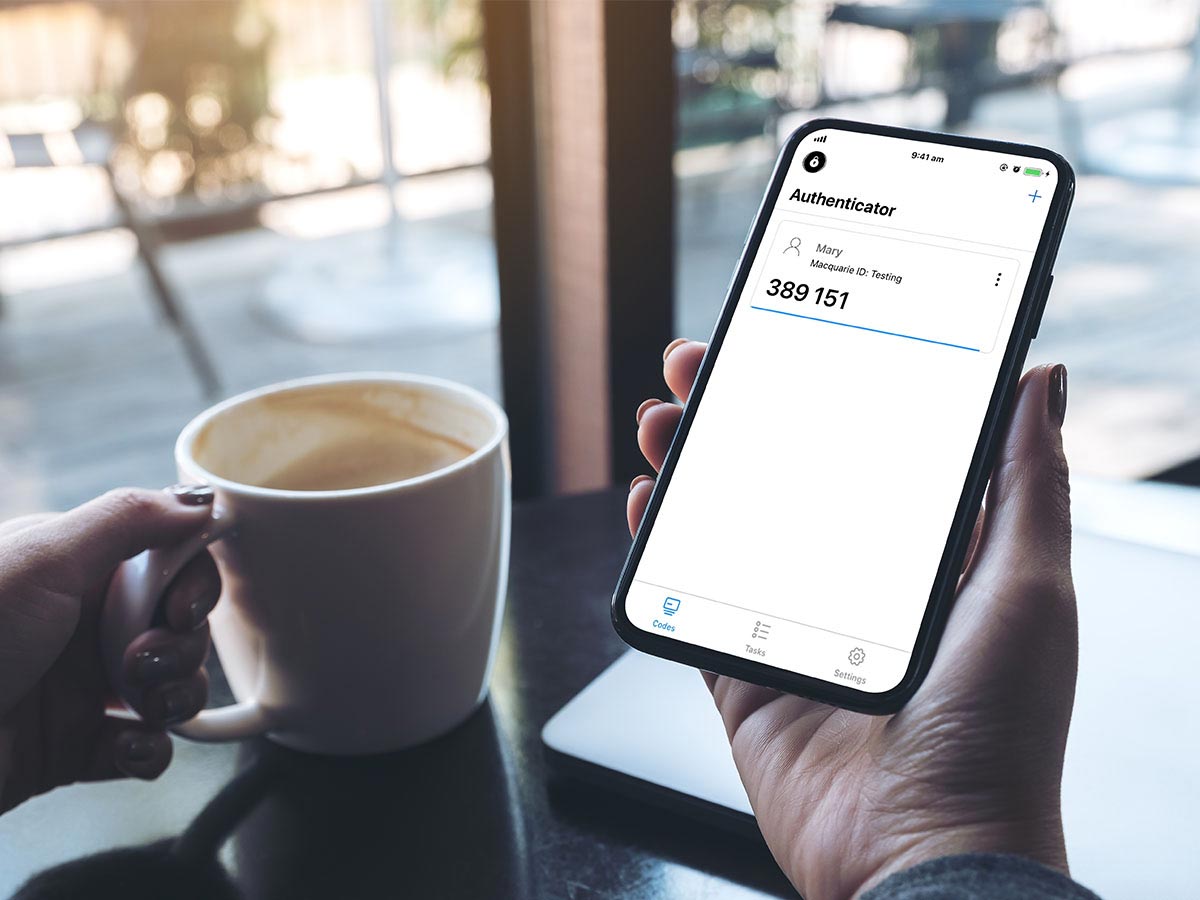 A person in a cafe close up shot of their hand holding a phone with the Macquarie authenticator app open