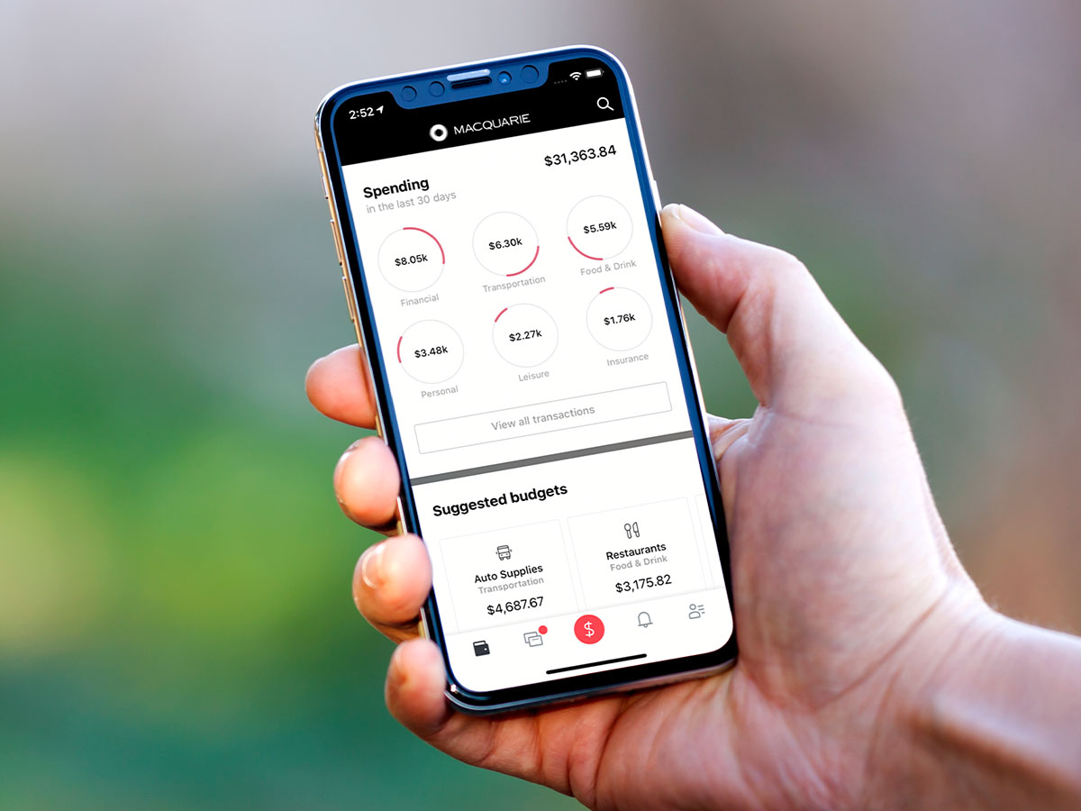 A hand holding a phone (iPhone X) with the Macquarie app open showing the spending and budgeting feature