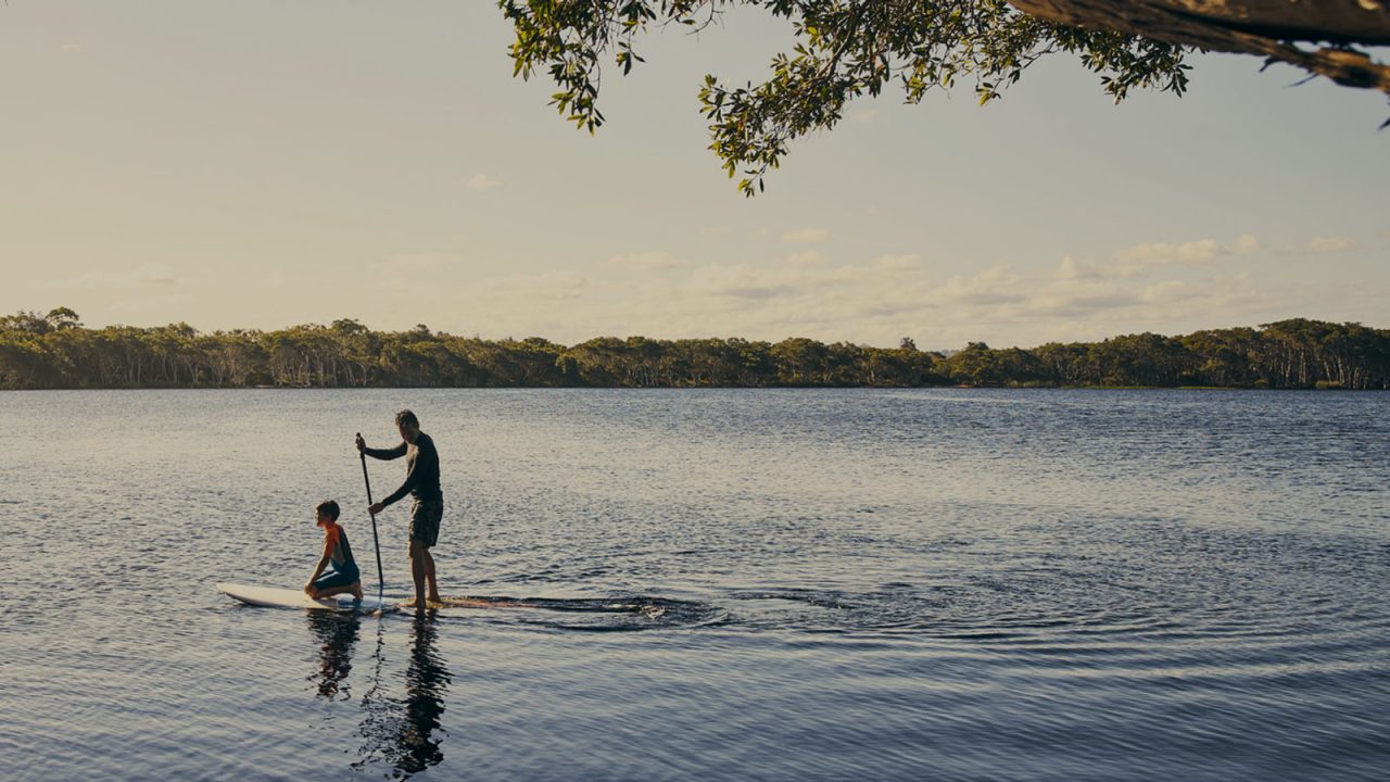 father and son paddling on lake with stand up paddle board
