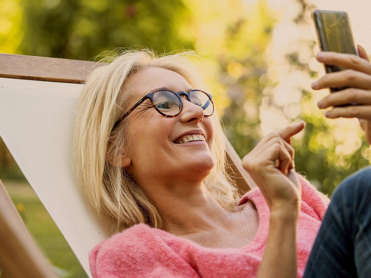 Smiling woman using smartphone while sitting on deckchair