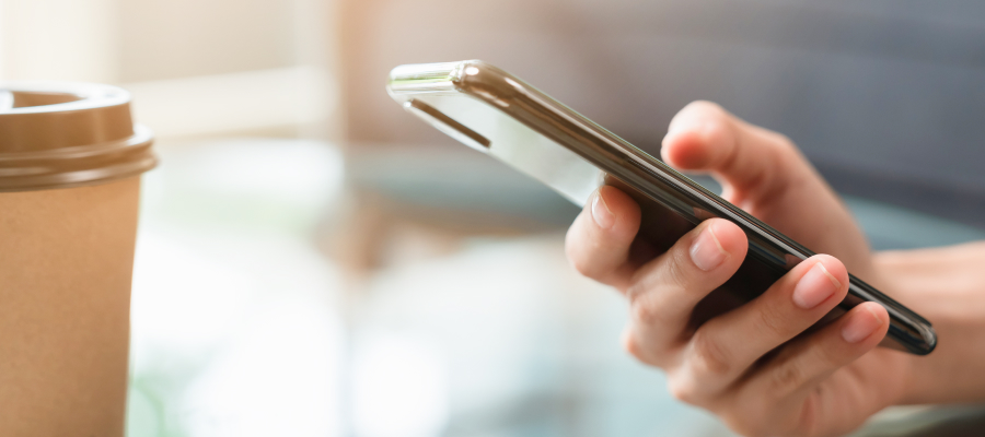 Image of a hand holding a phone and a coffee.