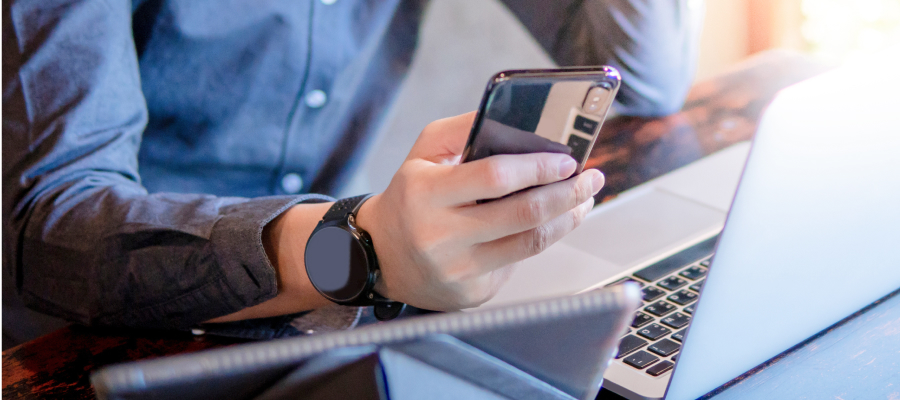 Image of a person holding a phone while looking at a laptop.