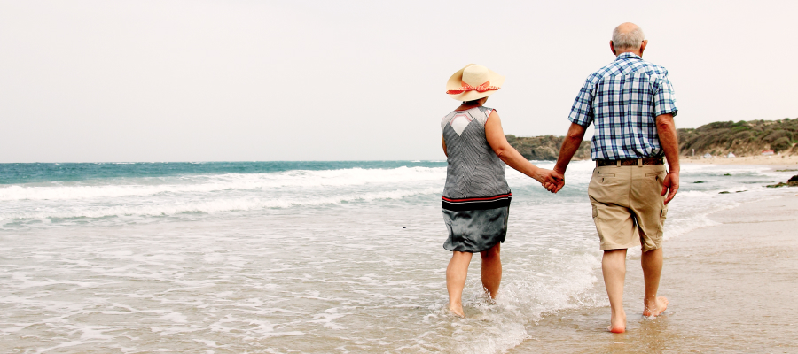 Image of an older couple holding hands and walking along a beach in the water.