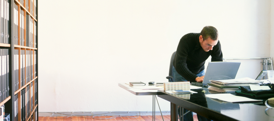 Image of a man standing in an office working on a laptop.