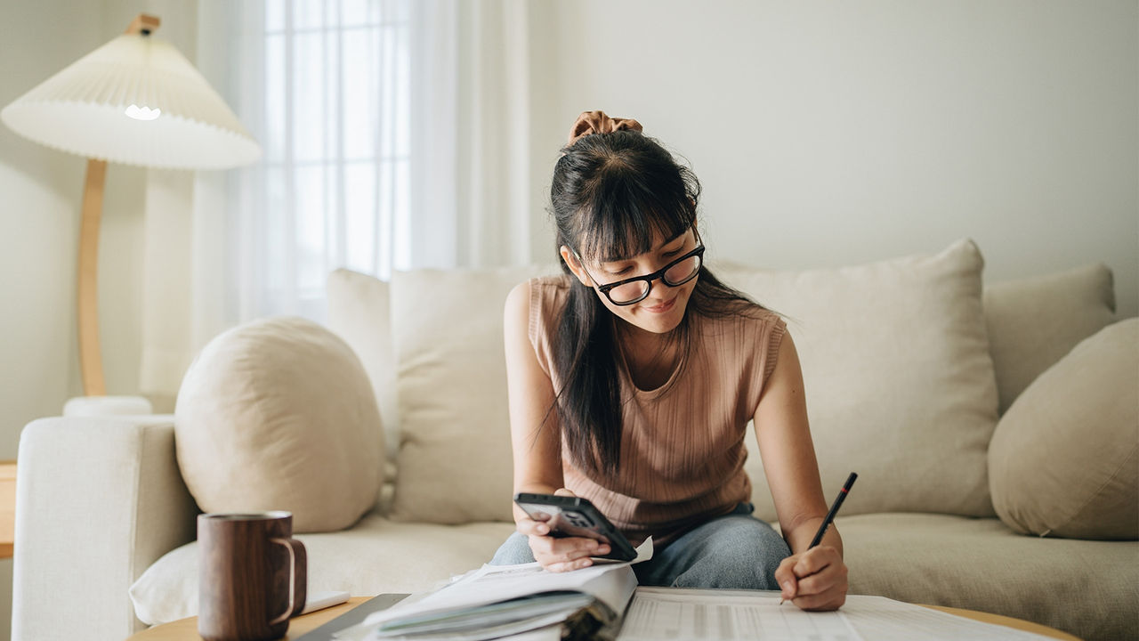 A young woman sitting on the sofa and writing notes.