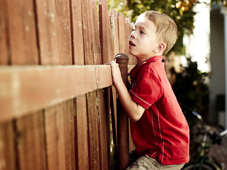 Little boy peeking over fence in backyard