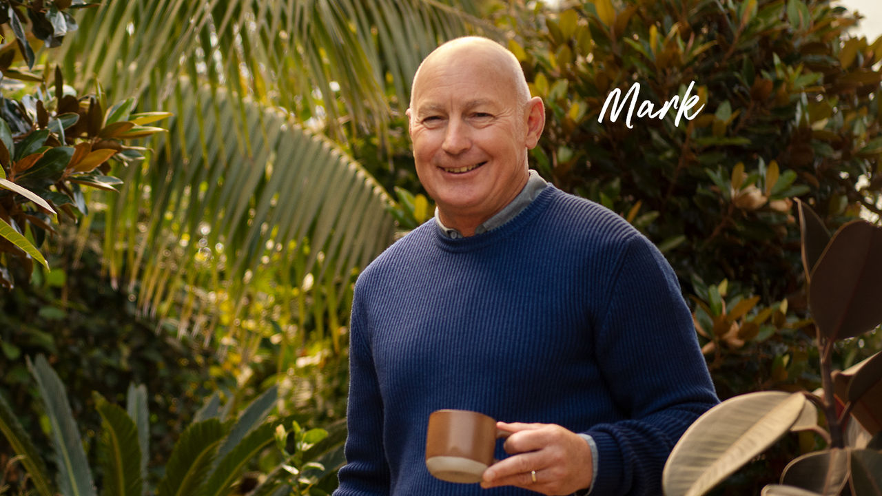 Mark a home loan customer smiling and holding mug in front of greenery outside