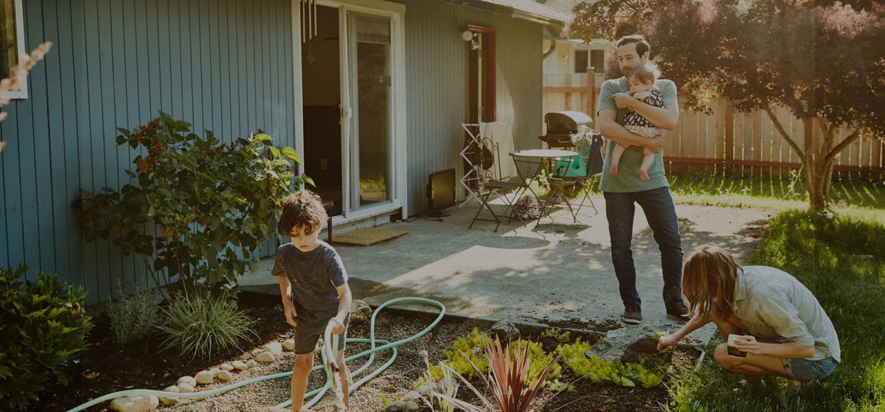 Family watering garden in backyard on summer morning