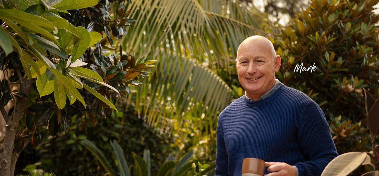 Mark a home loan customer smiling and holding mug in front of greenery outside
