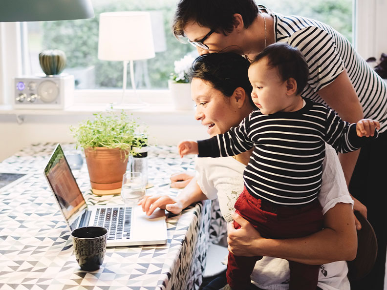 A same-sex couple with their child looking at a laptop in their kitchen.