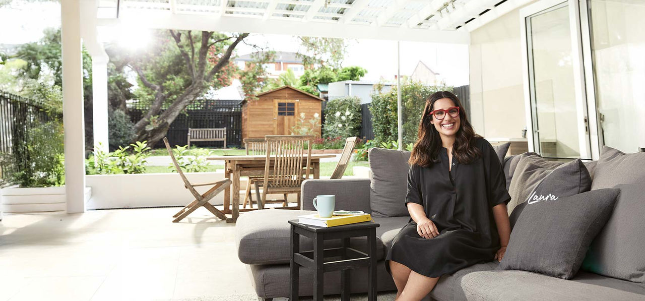 Laura, home loan customer, with red glasses sitting on couch in house smiling