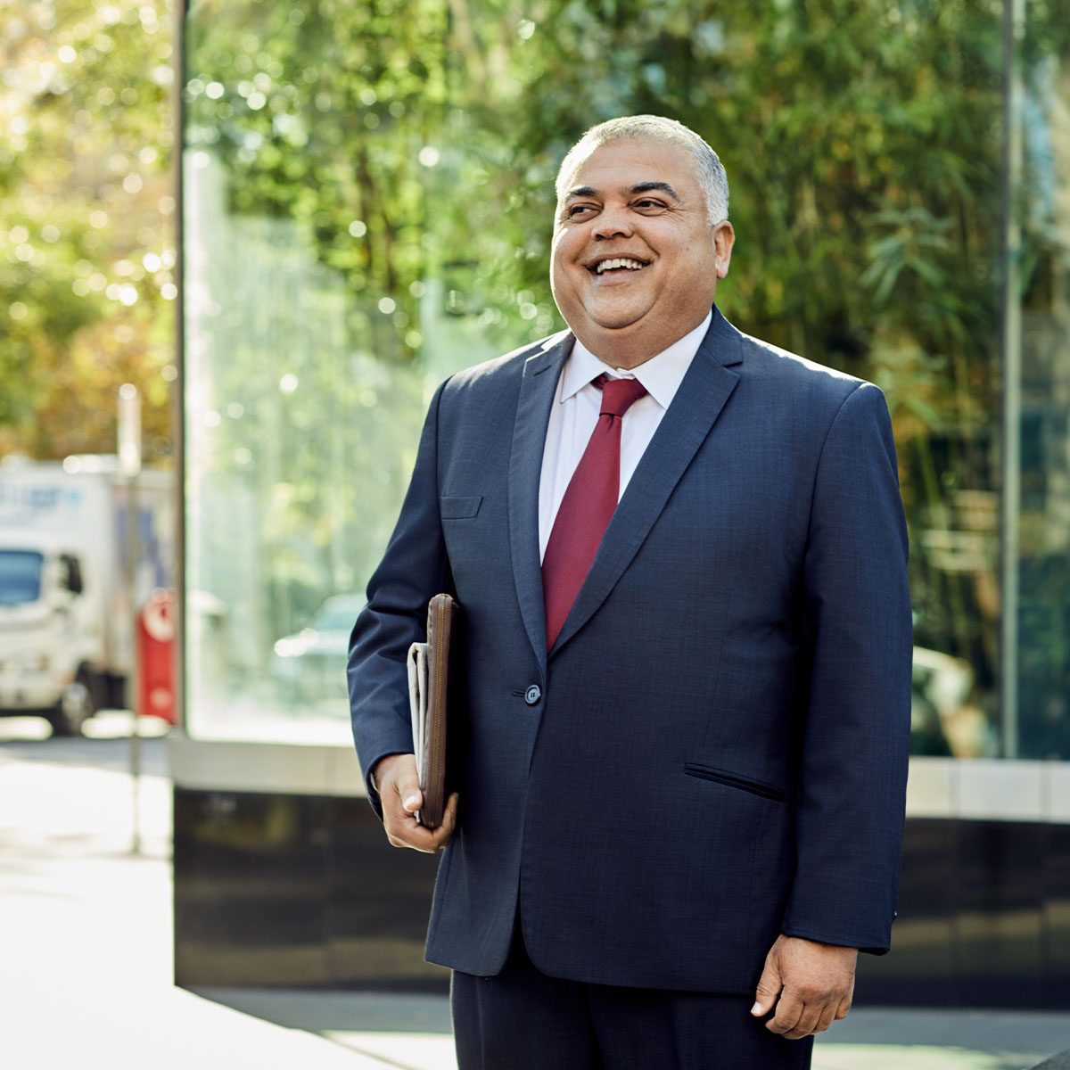 Professionally dressed business man smiling and standing outside while holding documents - Macquarie customer Francis
