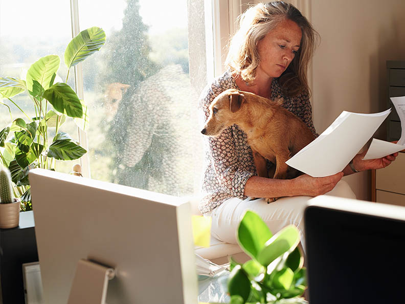 Woman with dog reviewing paperwork in sunny home office