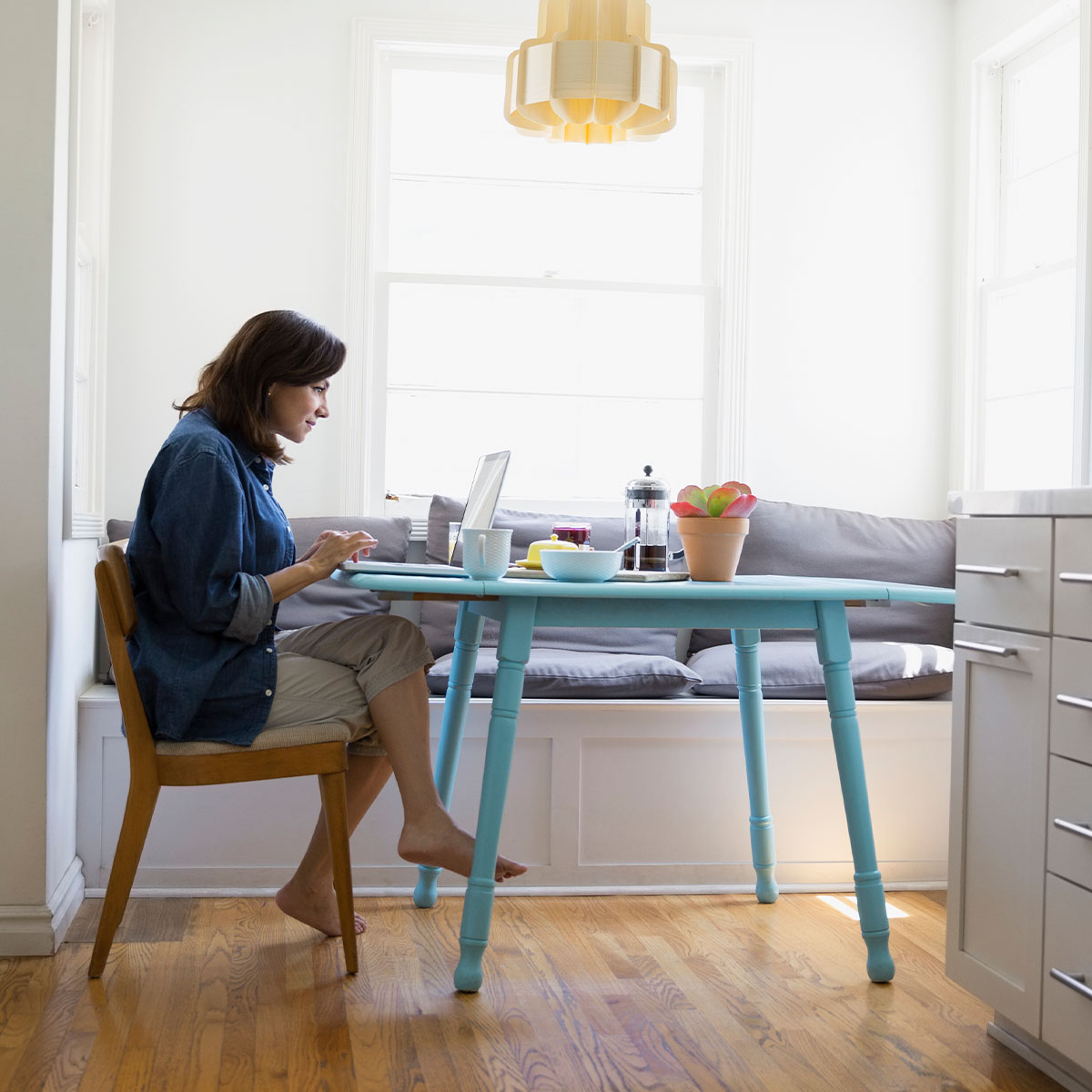 A medium shot of a woman sitting at a table in a breakfast book in her kitchen during the day.