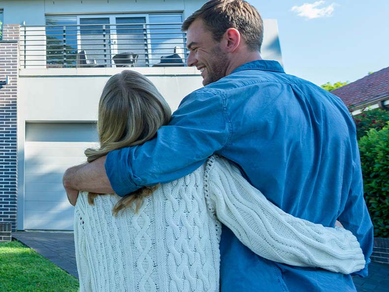 Couple hugging infront of modern house on a sunny day.