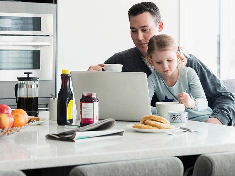 Father and daughter enjoying kitchen breakfast at laptop
