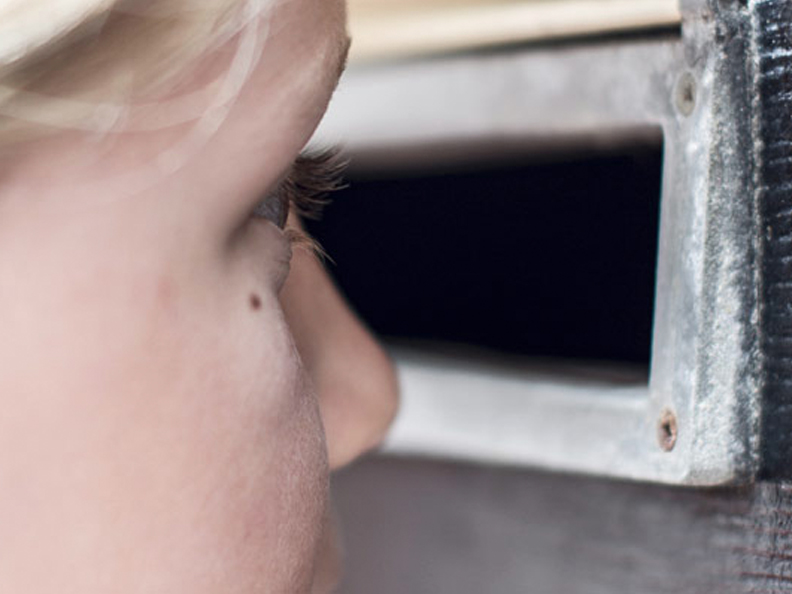 Little girl with blonde hair looking thru hole in letterbox.
