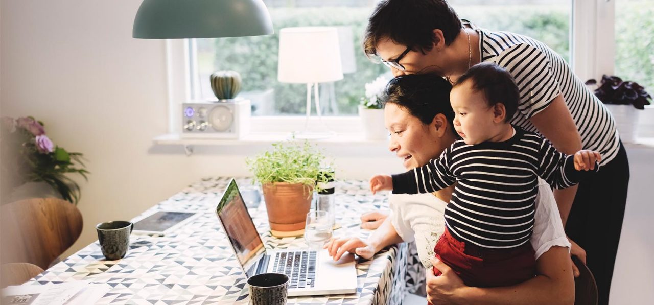 Lesbian couple with daughter looking in laptop at kitchen