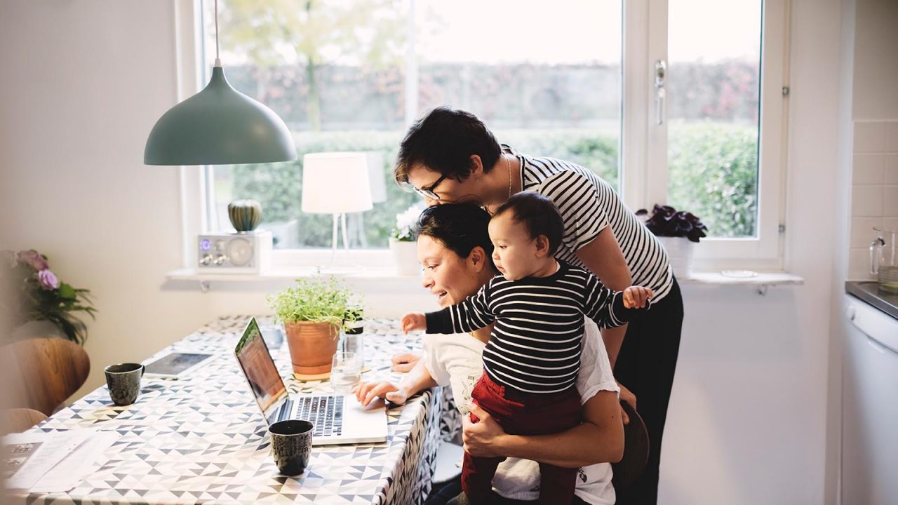 Lesbian couple with daughter looking in laptop at kitchen