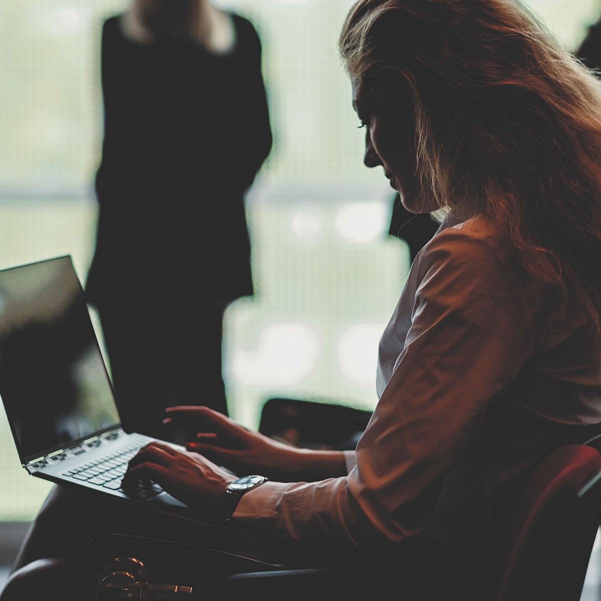 Business woman using a laptop in a conference room, they are in the shadows.