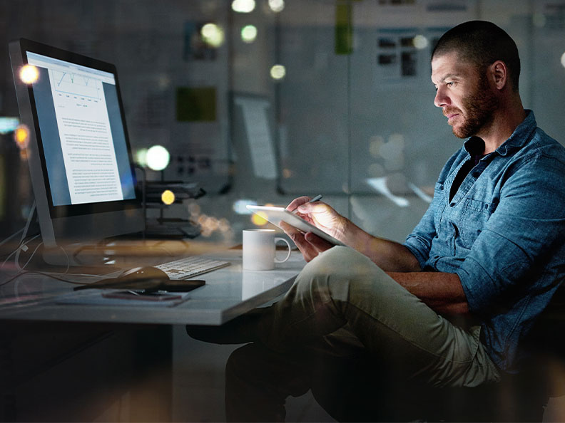 Shot of a businessman using a computer and digital tablet during a late night at the office