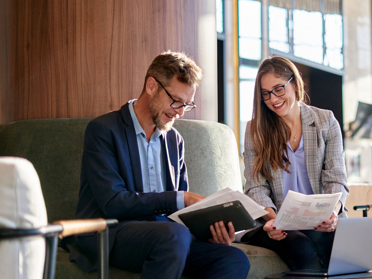 Two colleagues dressed professionally in business attire walk through their office talking.