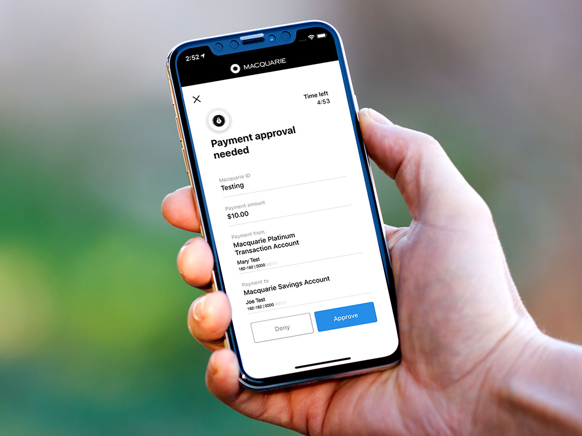 A hand holding a phone (iPhone X) with the Macquarie app open showing the spending and budgeting feature