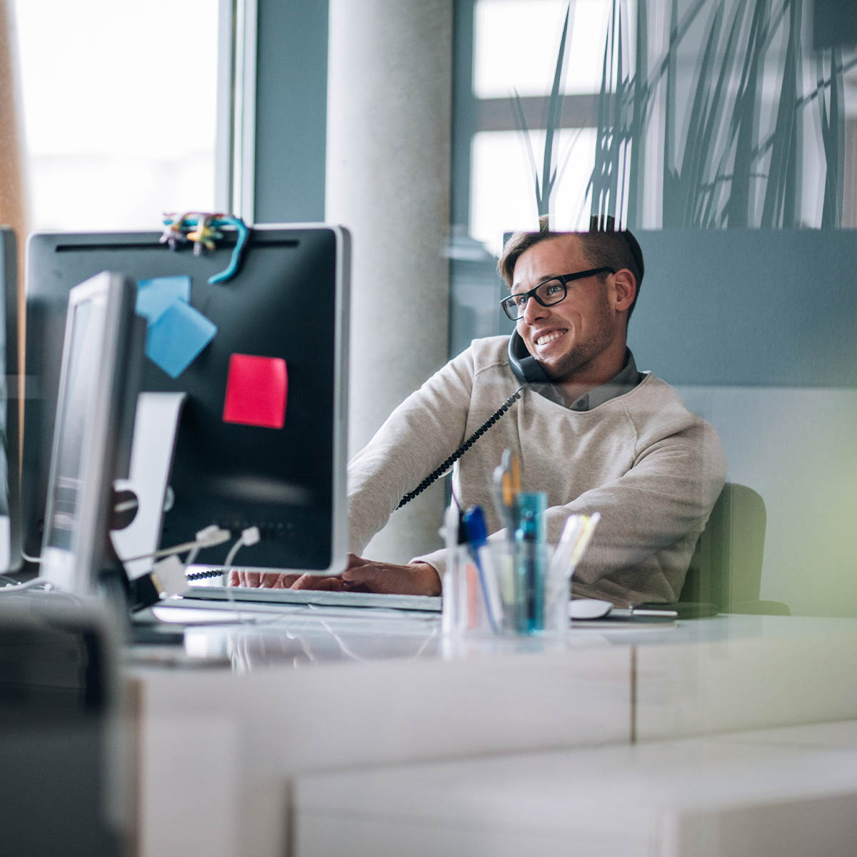 Business professional typing notes with keyboard on computer while talking and smiling on the phone to client.