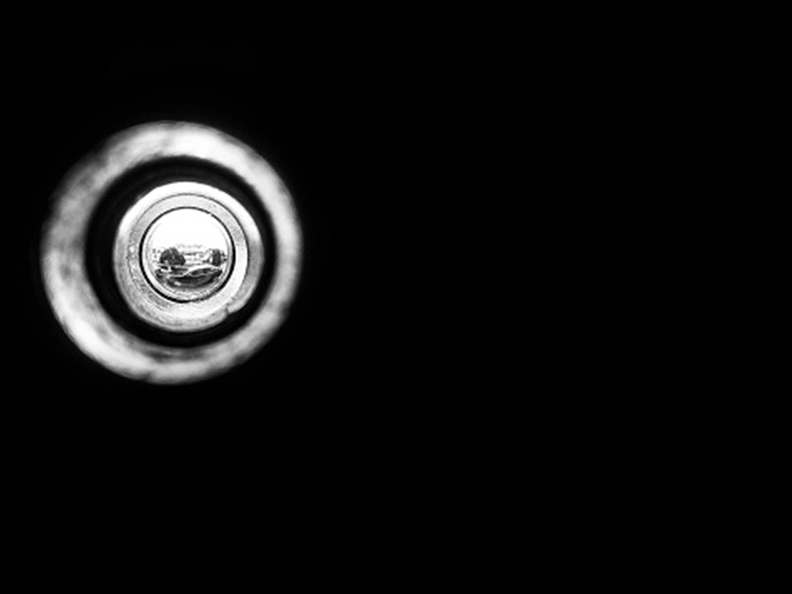 Black and white image. Abstract. Peeping through a door previewer to a streetscape.