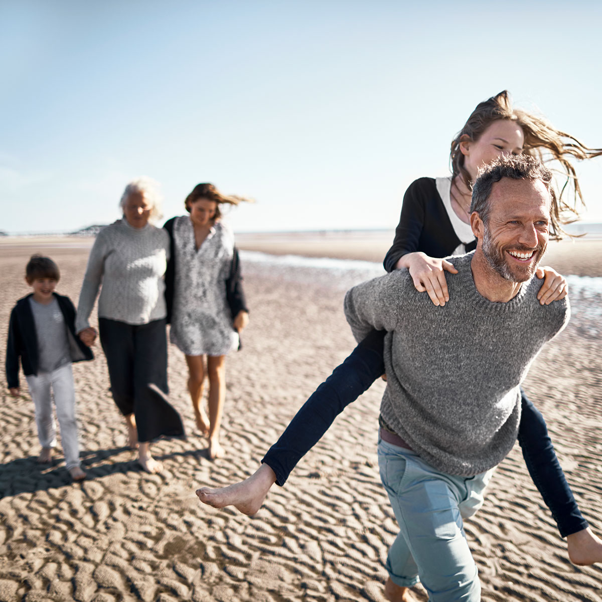 father and daughter oiggy backing on beach with family