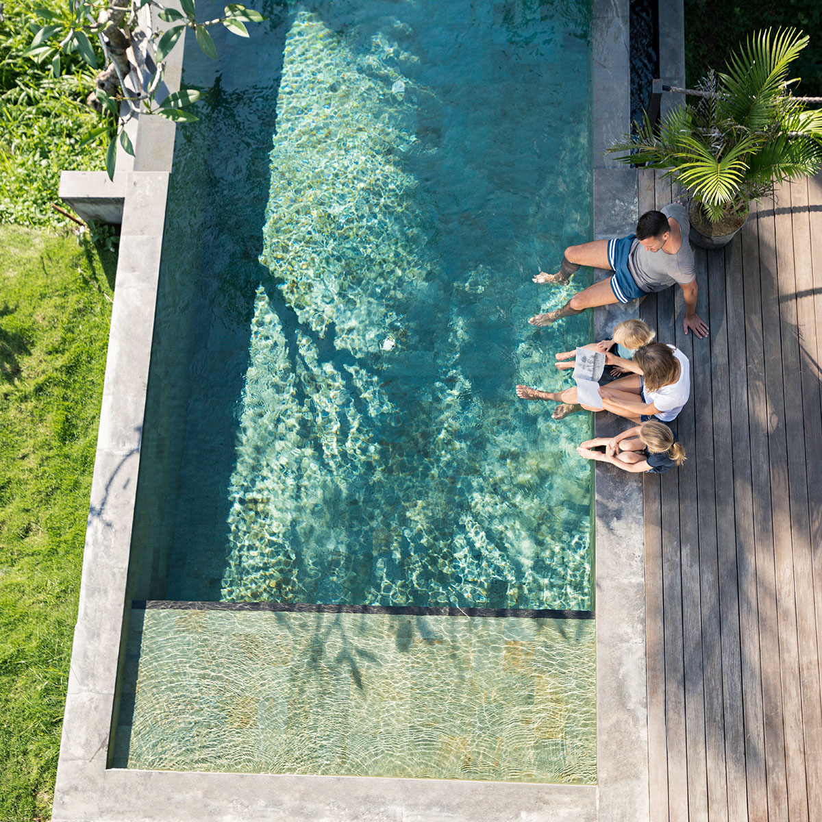 aerial shot of family dangling feet into residential pool