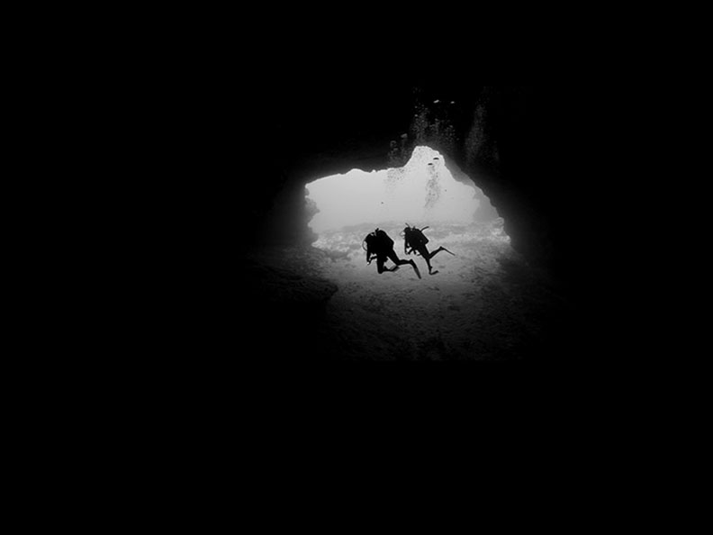 scuba divers swimming through cave