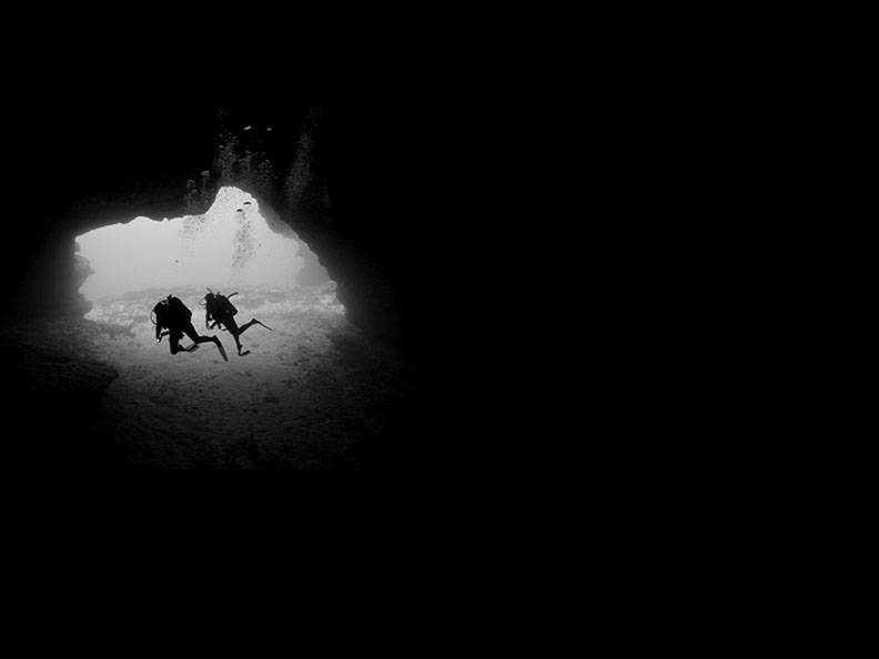 scuba divers swimming through cave