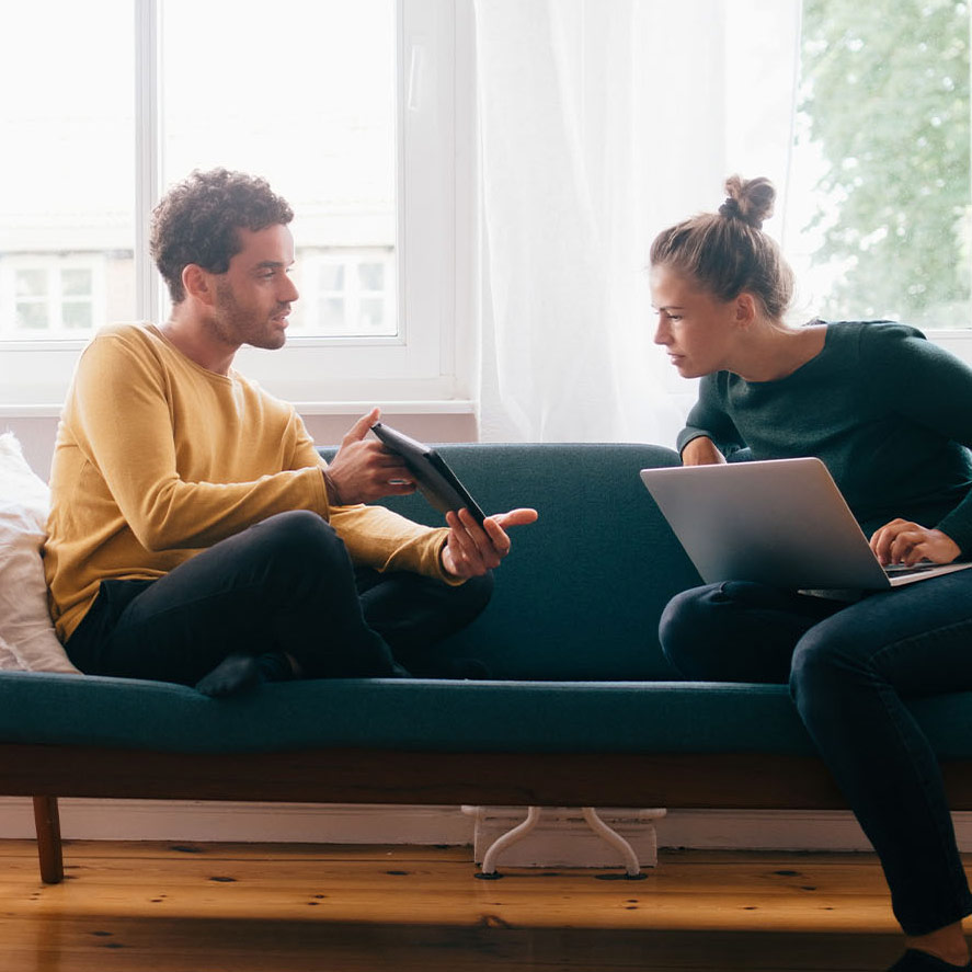 Boyfriend showing digital tablet to girlfriend while sitting on sofa at home 