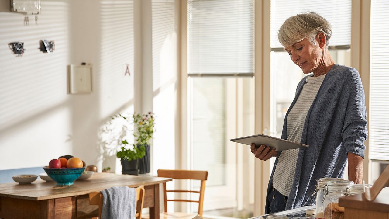 Senior woman standing in kitchen with digital tablet