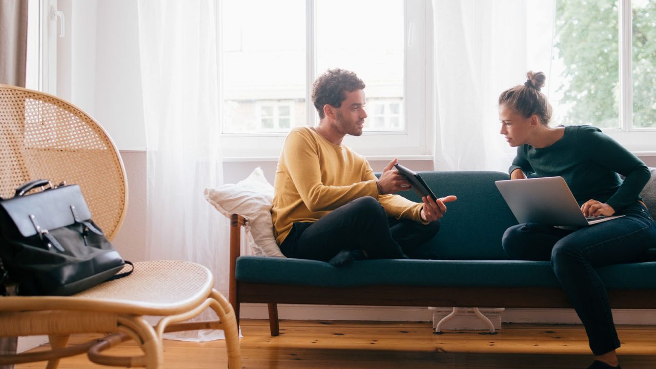 Boyfriend showing digital tablet to girlfriend while sitting on sofa at home 