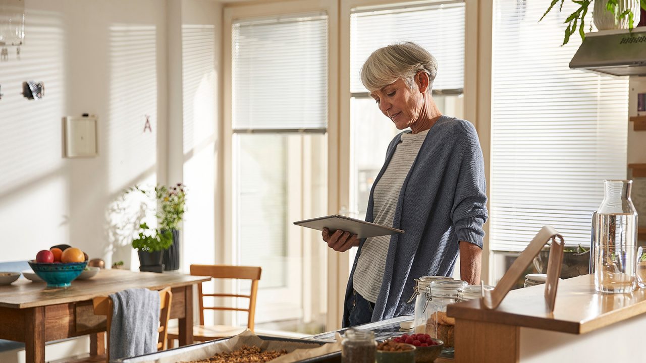 Senior woman standing in kitchen with digital tablet
