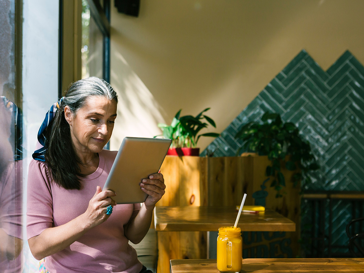 Woman holding digital tablet while leaning on window at cafe